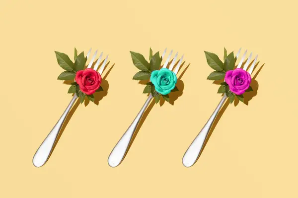 Metal çatallar, taze yapraklar ve renkli güllerle dekore edilmiş, estetik doğal düzen, pastel sarı arka plan, romantik yemek servisi fikri.