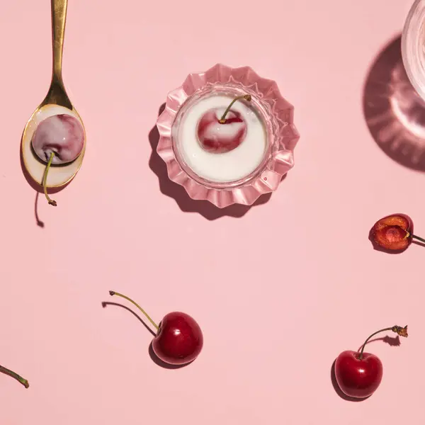 Yogurt fruit cup, a teaspoon and cherries, creative aesthetic delicious healthy snack serving, candy pink background.