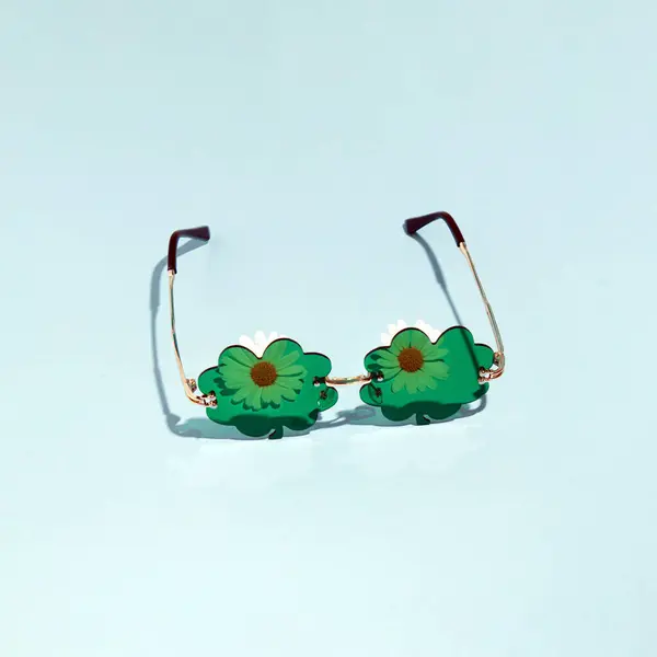 シャムロックの形をした緑のパーティーサングラスとデイジーな花 創造的な美学的な花のコンセプト パステルブルーの背景 セントパトリックのお祝いアイデア — ストック写真
