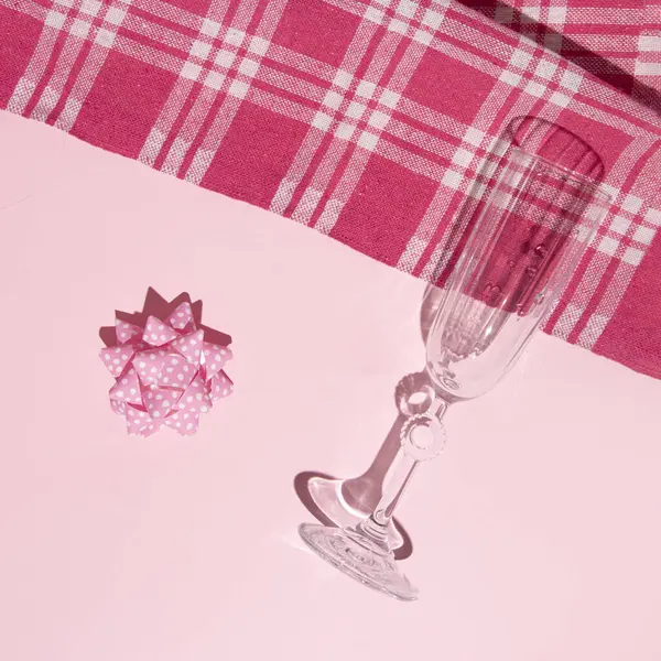 Şampanya flütü ve hediye yayı, minimal yaratıcı piknik fikri, retro tarzı, pastel pembe arka plan..