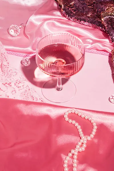 Şampanya kadehi, lüks kumaşlar, boncuklar ve kristaller, yaratıcı pastel pembe arka plan..