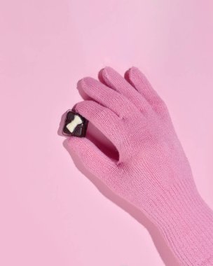 Yünlü eldivendeki bir el çikolata şekeri, kış tatili, pastel pembe desenli.