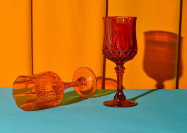 Deniz mavisi bir masada renkli şarap bardakları, kehribar kadife perde arka planı, retro estetik, sıcak renk paleti..