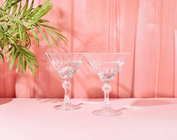 Two glasses of refreshing cocktails in the shade of a palm branch, pastel pink peach tulle curtain background, summer holiday romantic relax layout.