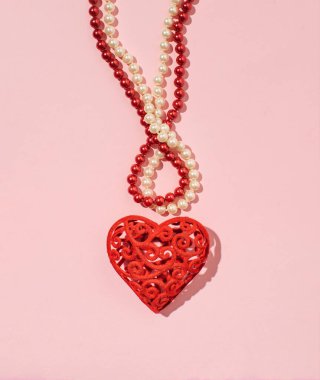 Kırmızı ve beyaz boncuklar, kalp şeklinde bir kolye ile dizilmiş, aşk ve romantizmden esinlenilmiş, pastel pembe arka planda bir süsleme.