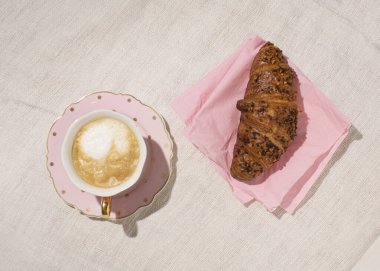 Bir fincan kapuçino ve taze pişmiş kruvasan organik masa örtüsü arka planda..