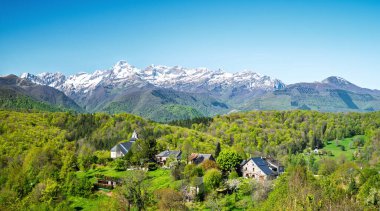 Baharda, arka planda karlı dağ sıraları olan Fransız dağ köyü.