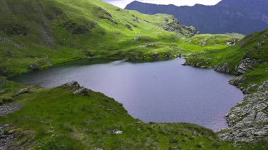 Romanya 'nın Fagaras Dağları' ndaki yeşil tepeler ve kayalık yamaçlarla çevrili dağ gölü. 