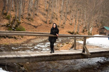 Sonbahar ormanında ceketli ve siyah ceketli genç bir kadın yürüyor.