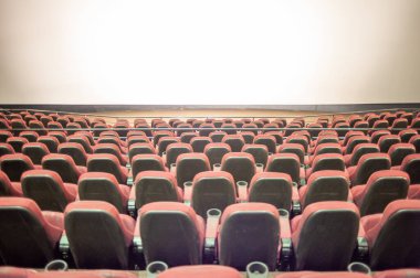 Boş sinema salonu, kırmızı koltuklar ve geniş bir pencere.
