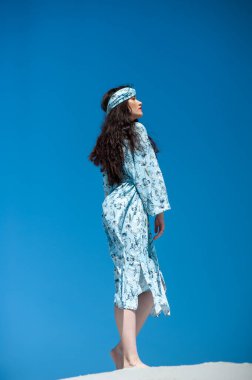 Mavi arka planda beyaz elbiseli güzel bir kadın.