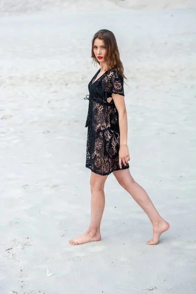 ビーチを歩いている黒いドレスの美しい女の子 — ストック写真