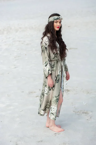 stock image beautiful young woman in a white dress and a hat with a backpack on the beach