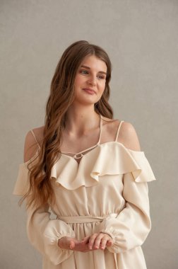 Gri arka planda beyaz elbiseli güzel bir kadın.