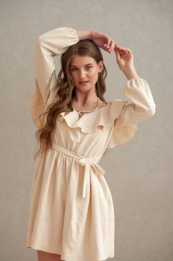 Gri arka planda beyaz elbiseli güzel bir kadın.