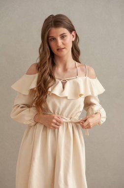 Gri arka planda bej elbiseli güzel bir kadın.