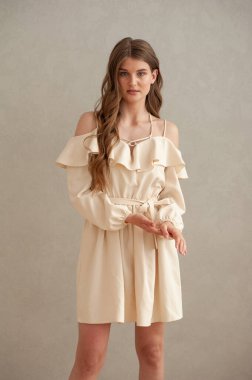 Gri arka planda bej elbiseli güzel bir kadın.