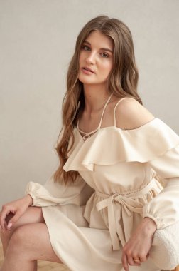 Güzel, genç, gülümseyen bir kadın portresi. Dalgalı saçlı. İç kısımda bej bir elbise giymiş. 