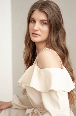 Güzel, genç, gülümseyen bir kadın portresi. Dalgalı saçlı. İç kısımda bej bir elbise giymiş. 