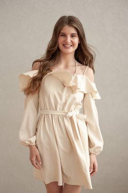 Güzel, genç, gülümseyen bir kadın portresi. Dalgalı saçlı. İç kısımda bej bir elbise giymiş. 