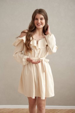 Güzel, genç, gülümseyen bir kadın portresi. Dalgalı saçlı. İç kısımda bej bir elbise giymiş. 