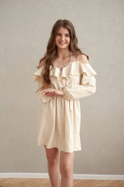 Güzel, genç, gülümseyen bir kadın portresi. Dalgalı saçlı. İç kısımda bej bir elbise giymiş. 