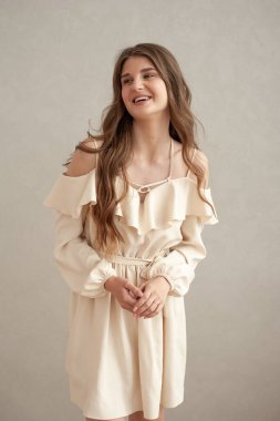 Güzel, genç, gülümseyen bir kadın portresi. Dalgalı saçlı. İç kısımda bej bir elbise giymiş. 