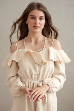 Güzel, genç, gülümseyen bir kadın portresi. Dalgalı saçlı. İç kısımda bej bir elbise giymiş. 