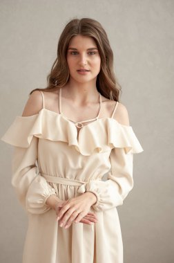 Güzel, genç, gülümseyen bir kadın portresi. Dalgalı saçlı. İç kısımda bej bir elbise giymiş. 