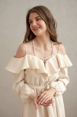 Güzel, genç, gülümseyen bir kadın portresi. Dalgalı saçlı. İç kısımda bej bir elbise giymiş. 