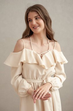 Güzel, genç, gülümseyen bir kadın portresi. Dalgalı saçlı. İç kısımda bej bir elbise giymiş. 