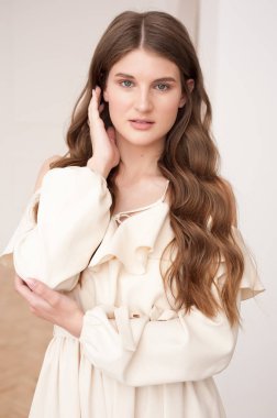 Güzel, genç, gülümseyen bir kadın portresi. Dalgalı saçlı. İç kısımda bej bir elbise giymiş. 