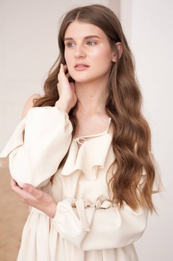 Güzel, genç, gülümseyen bir kadın portresi. Dalgalı saçlı. İç kısımda bej bir elbise giymiş. 