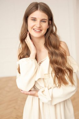 Güzel, genç, gülümseyen bir kadın portresi. Dalgalı saçlı. İç kısımda bej bir elbise giymiş. 