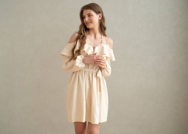 Güzel, genç, gülümseyen bir kadın portresi. Dalgalı saçlı. İç kısımda bej bir elbise giymiş. 