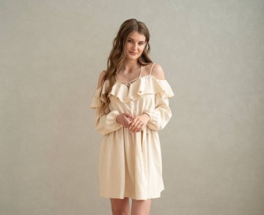 Güzel, genç, gülümseyen bir kadın portresi. Dalgalı saçlı. İç kısımda bej bir elbise giymiş. 