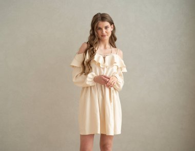 Güzel, genç, gülümseyen bir kadın portresi. Dalgalı saçlı. İç kısımda bej bir elbise giymiş. 