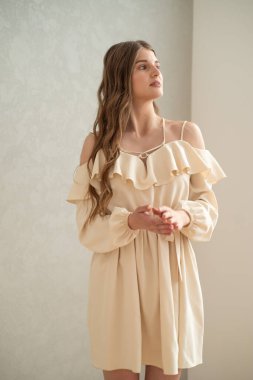 Güzel, genç, gülümseyen bir kadın portresi. Dalgalı saçlı. İç kısımda bej bir elbise giymiş. 