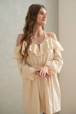 Güzel, genç, gülümseyen bir kadın portresi. Dalgalı saçlı. İç kısımda bej bir elbise giymiş. 