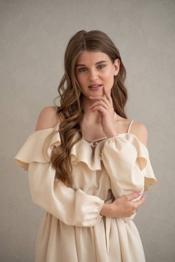 Güzel, genç, gülümseyen bir kadın portresi. Dalgalı saçlı. İç kısımda bej bir elbise giymiş. 