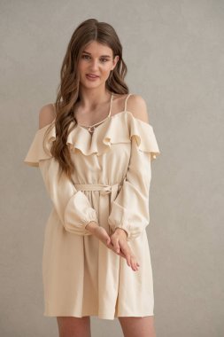 Güzel, genç, gülümseyen bir kadın portresi. Dalgalı saçlı. İç kısımda bej bir elbise giymiş. 