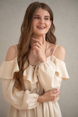 Güzel, genç, gülümseyen bir kadın portresi. Dalgalı saçlı. İç kısımda bej bir elbise giymiş. 