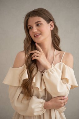 Güzel, genç, gülümseyen bir kadın portresi. Dalgalı saçlı. İç kısımda bej bir elbise giymiş. 