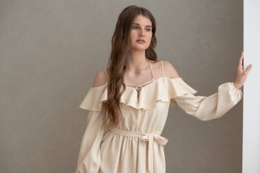 Güzel, genç, gülümseyen bir kadın portresi. Dalgalı saçlı. İç kısımda bej bir elbise giymiş. 