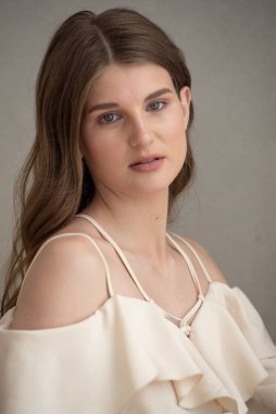 Güzel, genç, gülümseyen bir kadın portresi. Dalgalı saçlı. İç kısımda bej bir elbise giymiş. 