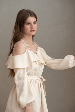 Güzel, genç, gülümseyen bir kadın portresi. Dalgalı saçlı. İç kısımda bej bir elbise giymiş. 