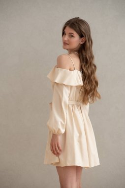 Güzel, genç, gülümseyen bir kadın portresi. Dalgalı saçlı. İç kısımda bej bir elbise giymiş. 