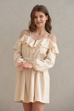 Güzel, genç, gülümseyen bir kadın portresi. Dalgalı saçlı. İç kısımda bej bir elbise giymiş. 