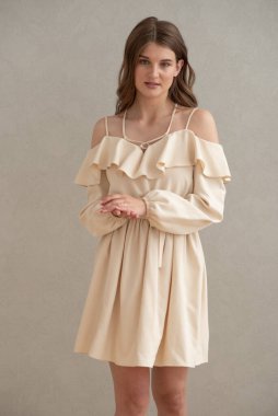 Güzel, genç, gülümseyen bir kadın portresi. Dalgalı saçlı. İç kısımda bej bir elbise giymiş. 