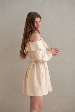 Güzel, genç, gülümseyen bir kadın portresi. Dalgalı saçlı. İç kısımda bej bir elbise giymiş. 